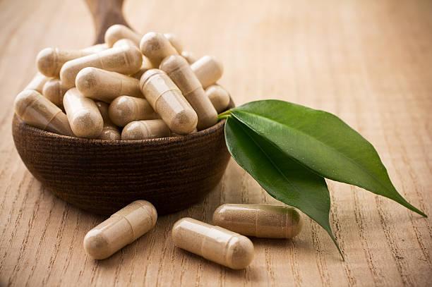 "Alternative medicine tablets on a wooden spoon, green leaf."